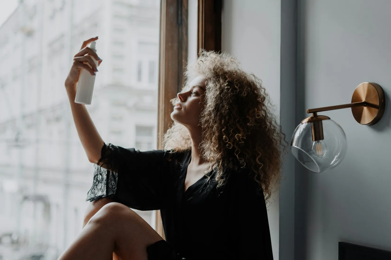 Woman spraying rose water on curly hair,